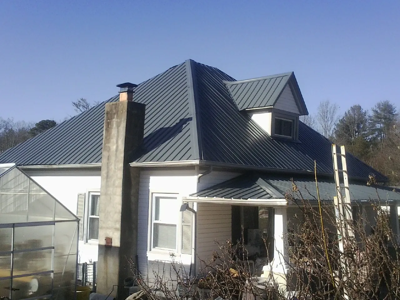 Dark blue standing seam metal roof on a white farmhouse with dormer — Slate & Tile Roof Repair by Roofing Brothers in Yancey