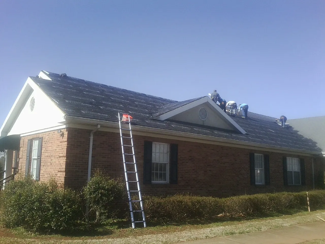 Crew tearing shingles off a brick ranch roof with a ladder set — Metal Roof Repair work by our crew in Yancey