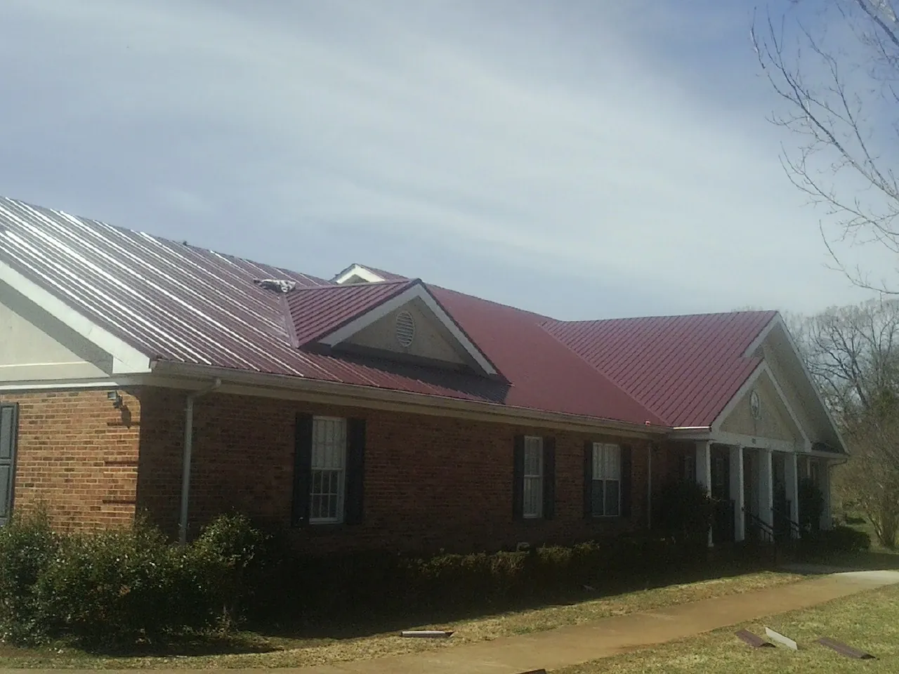 Red metal roof with gabled entries on a long brick building, from a Hail Damage Roof Repair job in Yancey