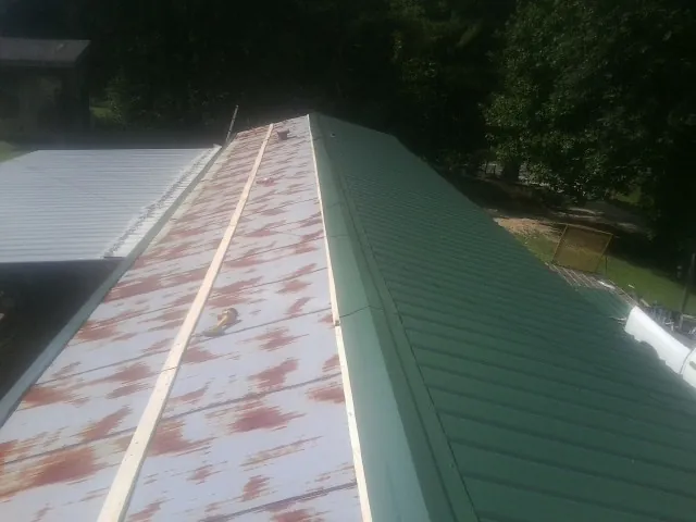 Old rusted panels beside newly installed green metal roofing — Wind Damage Roof Repair by Roofing Brothers in Yancey
