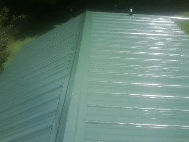 New green metal panels meeting at the ridge of a roof — Flat Roof Repair work by our crew in Yancey
