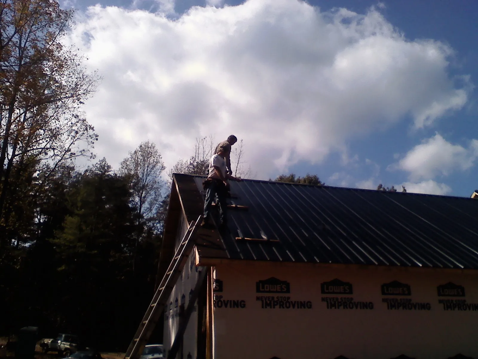 Roofer fastening dark metal panels high against a cloudy sky, from a Roof Inspection job in Yancey