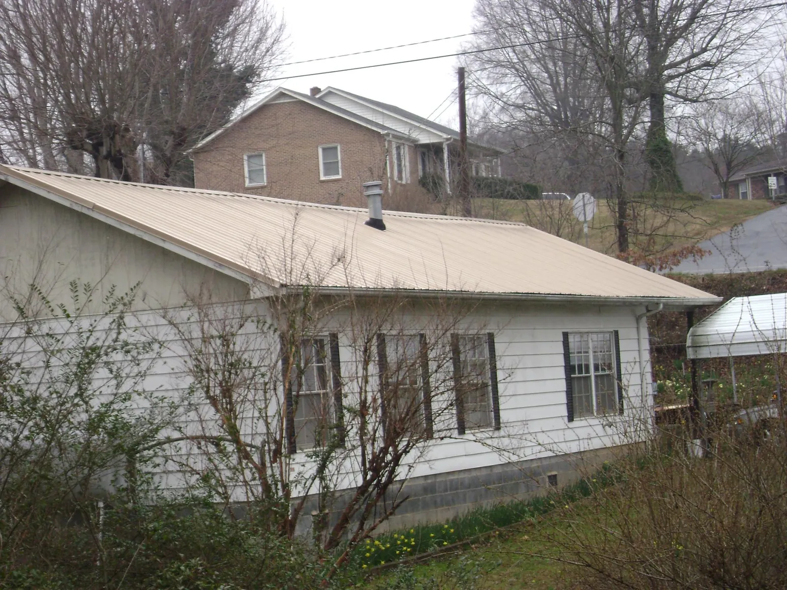Tan metal roof on a white sided house set into a hillside — Commercial Roofing by Roofing Brothers in Yancey
