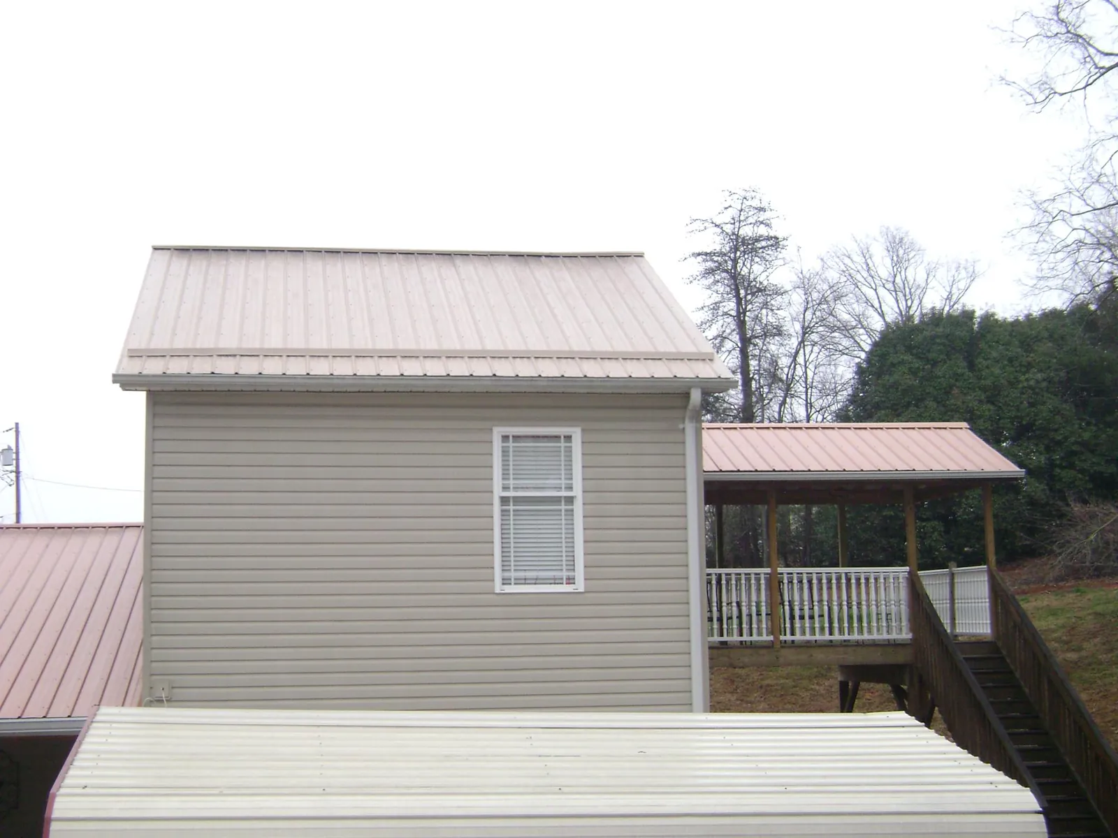 Tan metal roofs on a two story addition and attached porch, from a Roof Replacement job in Yancey